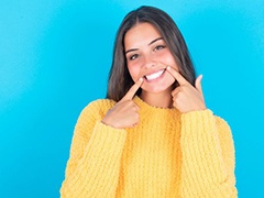 Woman in yellow sweater pointing at her teeth