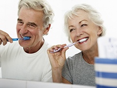 An older couple standing in front of their bathroom mirror and brushing their teeth in Torrance