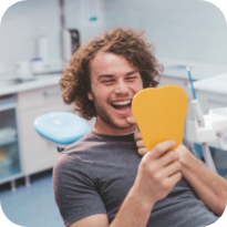 Young man in dental chair looking at his smile in a mirror