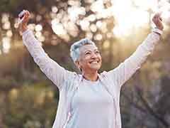 An older, confident woman smiling outdoors and raising her arms