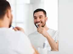 A man brushing his teeth while facing a bathroom mirror