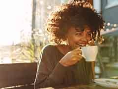 Woman smiling while drinking cup of coffee outside