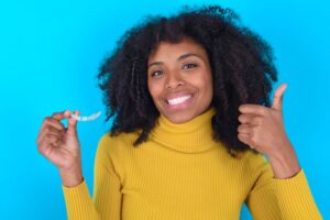 Smiling woman holding clear aligner and making thumbs-up gesture