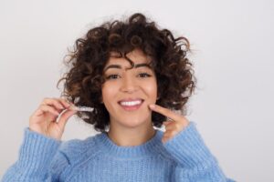 Woman in sweater holding Invisalign aligner